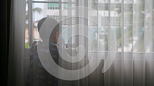 a boy behind the curtain is looking at the view in the window