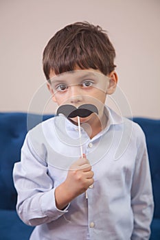 Boy with big eyes plays with a paper toy black mustache