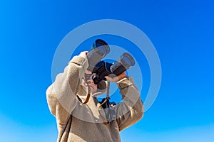 A boy with binoculars on a background of blue sky looks up