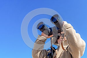A boy with binoculars on a background of blue sky looks up