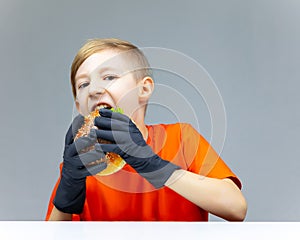 A boy in black disposable gloves grabbed a burger and wants to bite it greedily