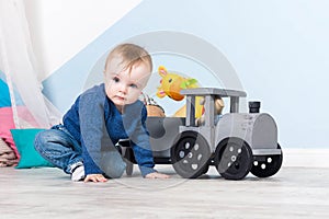 Boy blond in a blue sweater sits on a wooden floor. One year old baby playing with wooden toys.  train made of wood, with girafe