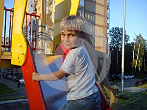 A boy with blond hair climbed a hill on the playground, turns back, smiles and frowns. Gaming equipment for the street. Bright red