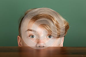 Boy with blond quiff looking over desk