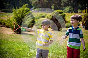 Boy blowing soap bubbles while an excited kid enjoys the bubbles. Happy teenage boy and his brother in a park enjoying making soap