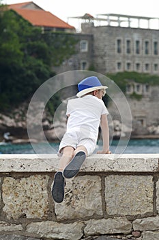 boy in a blue hat leaned over the parapet and looks thoughtfully