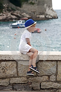 boy in a blue hat sits with his leg folded on the parapet and lo