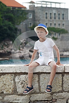 boy in a blue hat sits with his leg folded on the parapet and lo