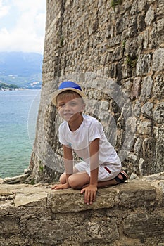 boy in a blue hat sitting on parapet of the ancient fortress of