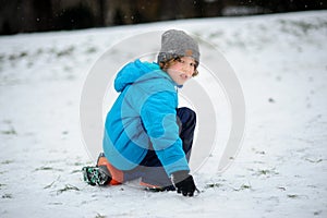 The boy in a blue jacket alone sits on snow.