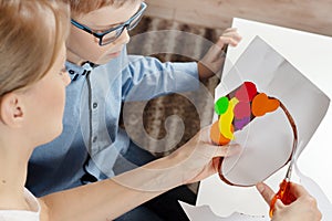 Boy in a blue shirt with mum. The boy`s mom cuts scissors with a plastic work done by a child.