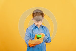 A boy in a blue shirt and orange gloves examines a green washing sponge