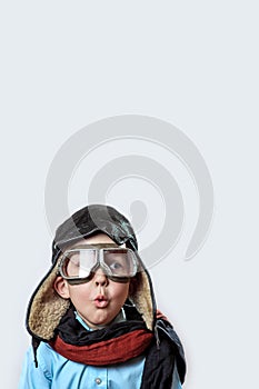 Boy in a blue shirt, pilot`s glasses, hat and scarf on a light background