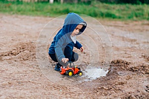 The boy in blue suit plays with a toy car in the dirt