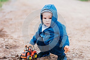 The boy in blue suit plays with a toy car in the dirt