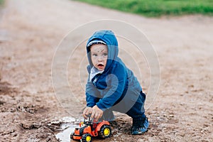 The boy in blue suit plays with a toy car in the dirt