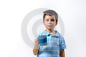 A boy in a blue T-shirt drinks with a blue cup stands on a light background