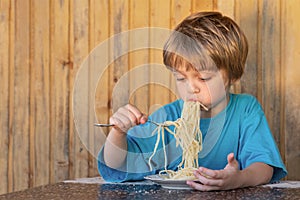 A boy in a blue t-shirt, is greedy eating spaghetti