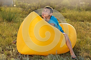 Boy in a blue t-shirt, sitting on a yellow lamzak, in nature, the concept of summer