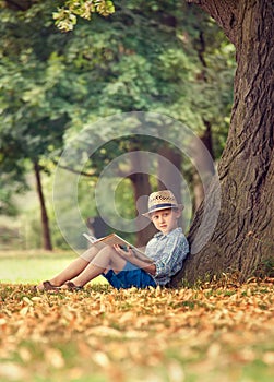 Boy with book sitting under big tree in park