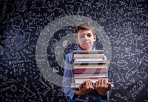 Boy with books against big blackboard with mathematical symbols