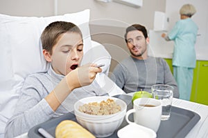 boy with breakfast in bed in hospital with father