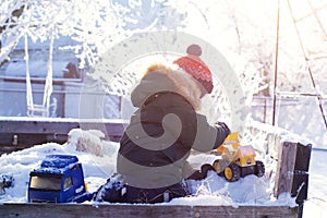 A boy in a bright orange hat plays with toys in a snowy winter Park