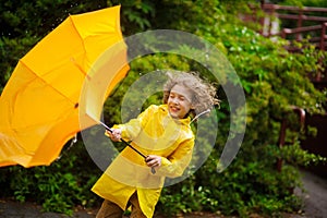 The boy in a bright yellow raincoat with effort holds an umbrella from wind.