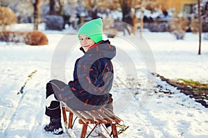 Boy with broken hand outdoors in winter park. Cute kid with broken arm and gypsum sitting on sled