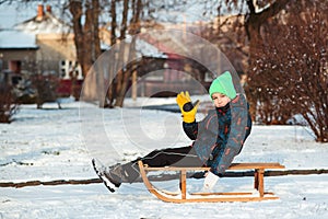 Boy with broken hand outdoors in winter park. Cute kid with broken arm and gypsum sitting on sled