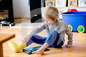 Boy with broken leg in cast playing on tablet.