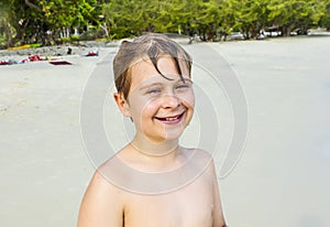 Boy with brown wet hair is smiling and enjoying the beach