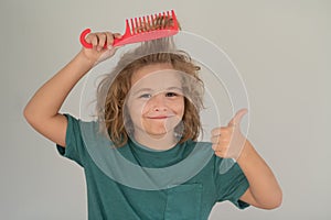 Boy brushes his hair. Cute child with comb. Blonde kid combs unruly hair. Kid boy with tangled long hair.