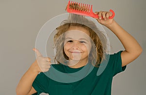 Boy brushes his hair. Cute child with comb. Blonde kid combs unruly hair. Kid boy with tangled long hair.
