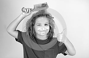 Boy brushes his hair. Cute child with comb. Blonde kid combs unruly hair. Kid boy with tangled long hair.