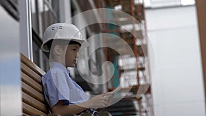 Boy builder sits on the bench uses a tablet, monitors the builder project, plays a builder