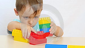 A boy builds out of colored blocks of a constructor at a table on a white background.