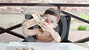 Boy built a toy plane of wood and is playing with it. Child in the workshop makes crafts