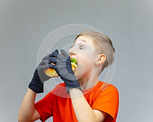 The boy bulged his eyes and bites a huge juicy burger with a salad inside
