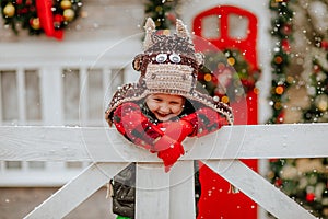 Boy in bull hat and red gloves posing up white fence and making funny faces