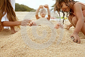 Boy Buried In Sand On Beach. Mother And Little Sister Playing On Coast. Family Enjoying Summer At Tropical Resort.