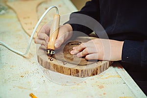 Boy burn out numbers with soldering iron on wooden disc. Kid makes wooden clock in the workshop