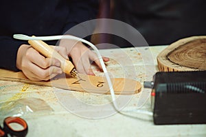 Boy burn out numbers with soldering iron on wooden disc. Kid makes wooden clock in the workshop