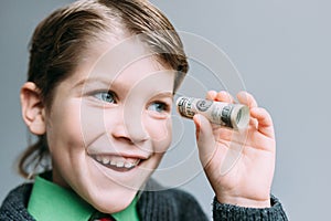 Boy businessman looks through small tube from dollar