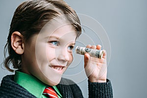 Boy businessman looks through small tube from dollar