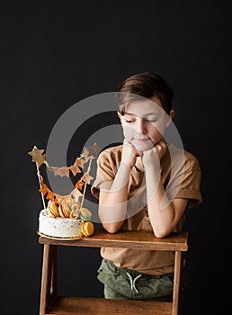 a boy with a cake, he has a birthday, a boy wearing a beige t-shirt and green pants on a black background