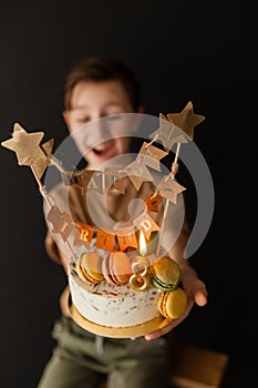 a boy with a cake, he has a birthday, a boy wearing a beige t-shirt and green pants on a black background