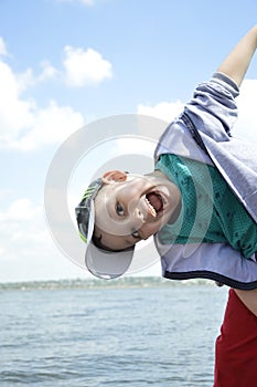 boy in a cap against a background of water and blue sky with white clouds