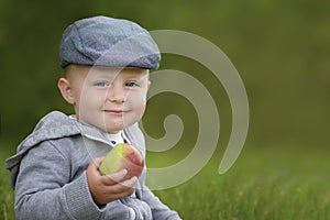 Boy in cap with apple in hand looking at camera