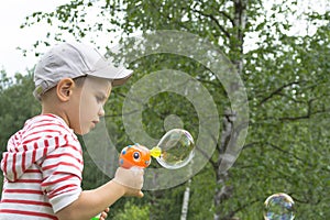 The boy in the cap lets soap bubbles in the summer against the background of green birches